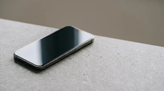 Smartphone moderne posé sur surface minérale avec reflets subtils, écran impeccable sans rayures